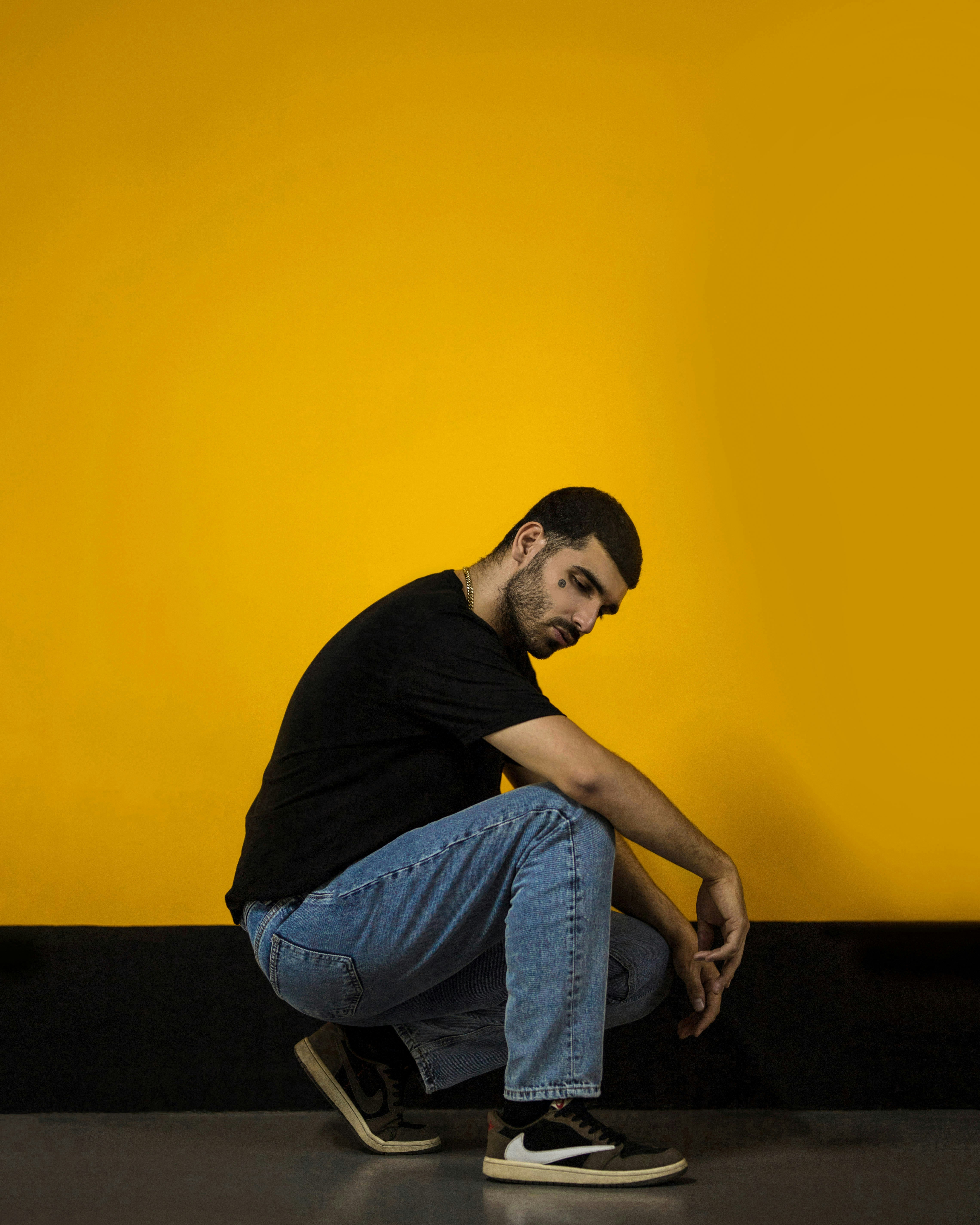 man in black shirt and blue denim jeans sitting on yellow wall